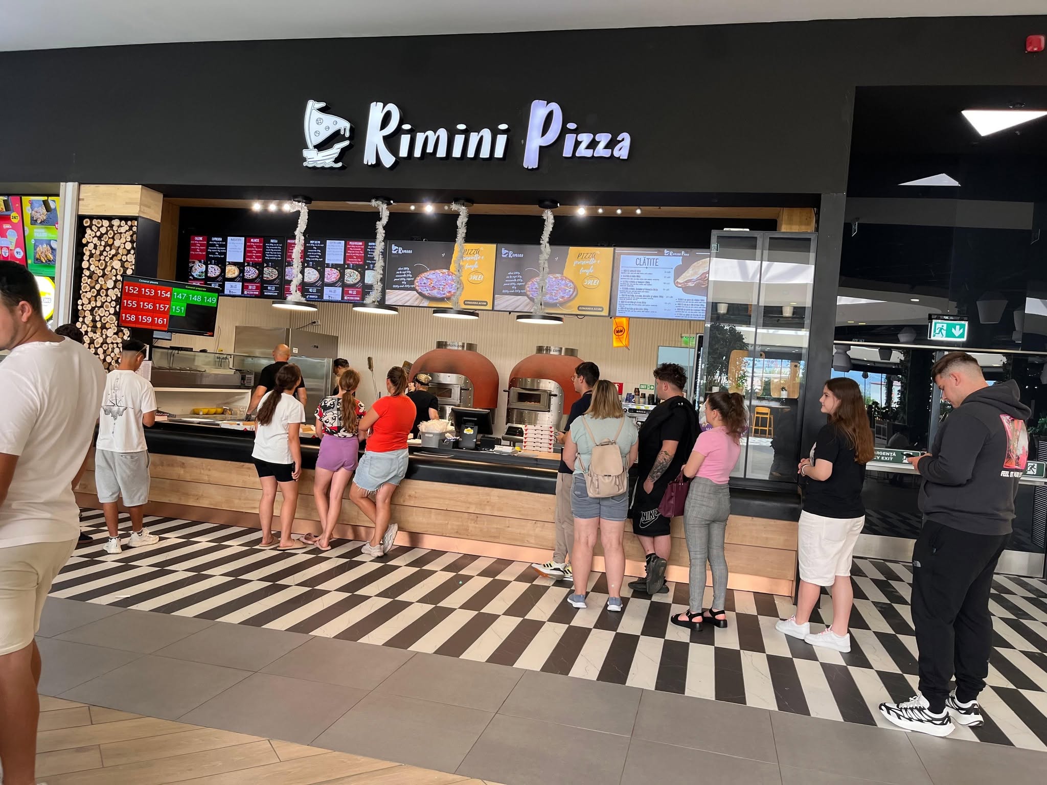 Interior călduros al Pizzeriei Rimini cu pereți din cărămidă și lumini suspendate